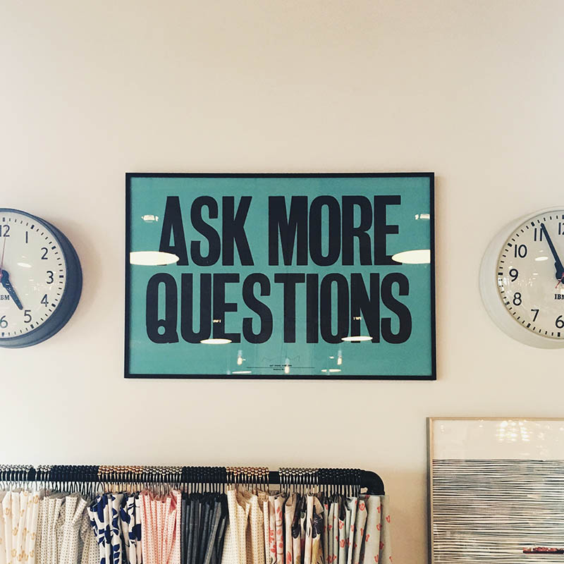 2つのアナログ時計の間の壁にあるオールキャップスの「ASKMOREQUESTIONS」と書かれた看板。