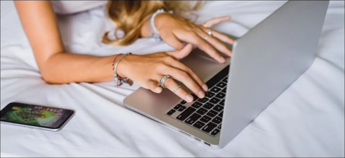 Kobieta korzystająca z MacBooka na łóżku, które źle wpływa na chłodzenie.