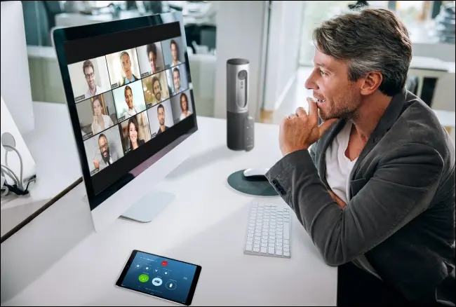 Мужчина на собрании Zoom на своем Mac с участниками в режиме галереи на мониторе.