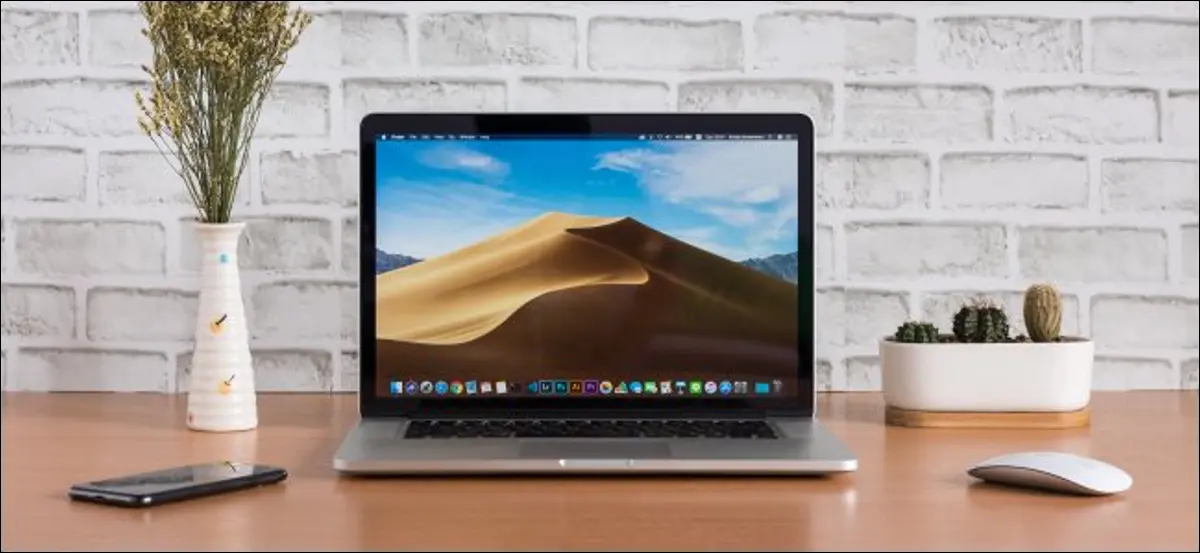 マウスとスマートフォンの隣の机の上に座っている開いたMacBook。