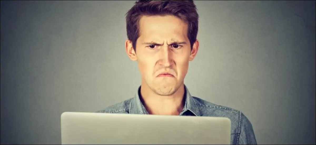 MacBookの画面で眉をひそめている男。