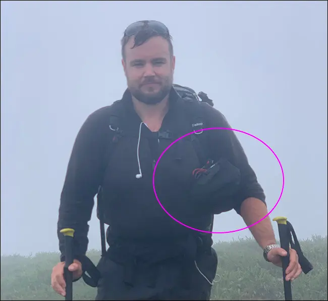 Un bărbat care merge în ploaie purtând un trepied și o geantă Peak Design Camera Shell.
