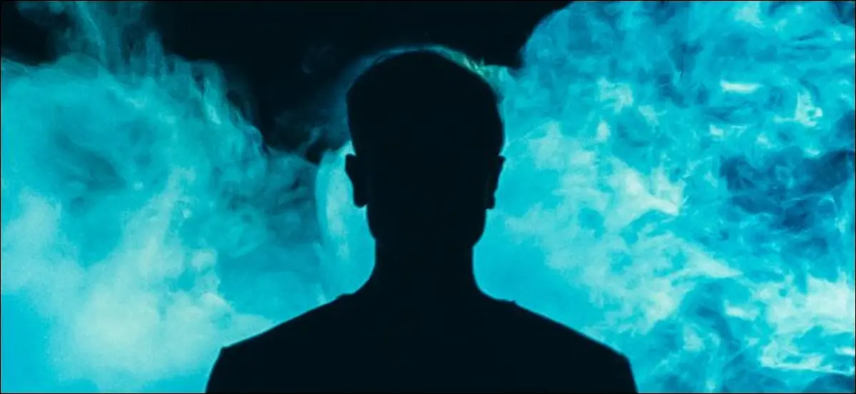 Eine Silhouette einer Person vor blauem Rauch auf dunklem Hintergrund.