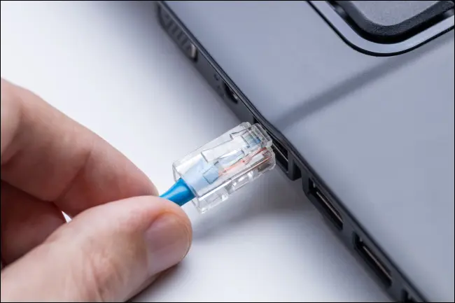 Una mano che collega un cavo Ethernet a un laptop.