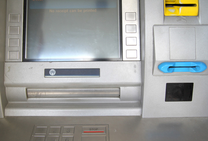 Un dispozitiv de plastic galben pe un bancomat care conține un skimmer