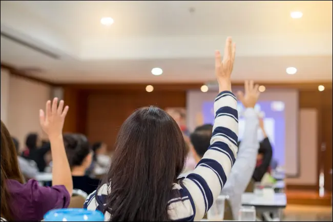 Oameni de afaceri care ridică mâinile pentru a pune întrebări într-o conferință.