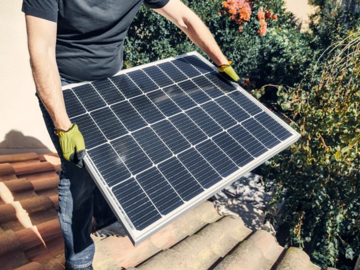 uma pessoa de camisa preta segurando um painel solar em pé no telhado