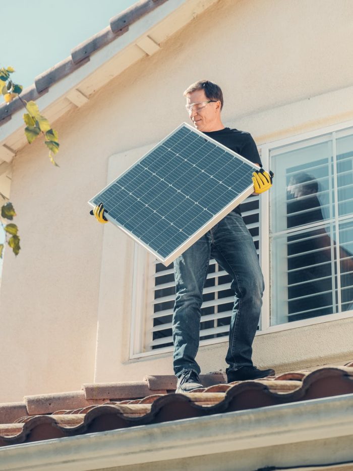 um homem de camisa preta em pé no telhado enquanto segura um painel solar