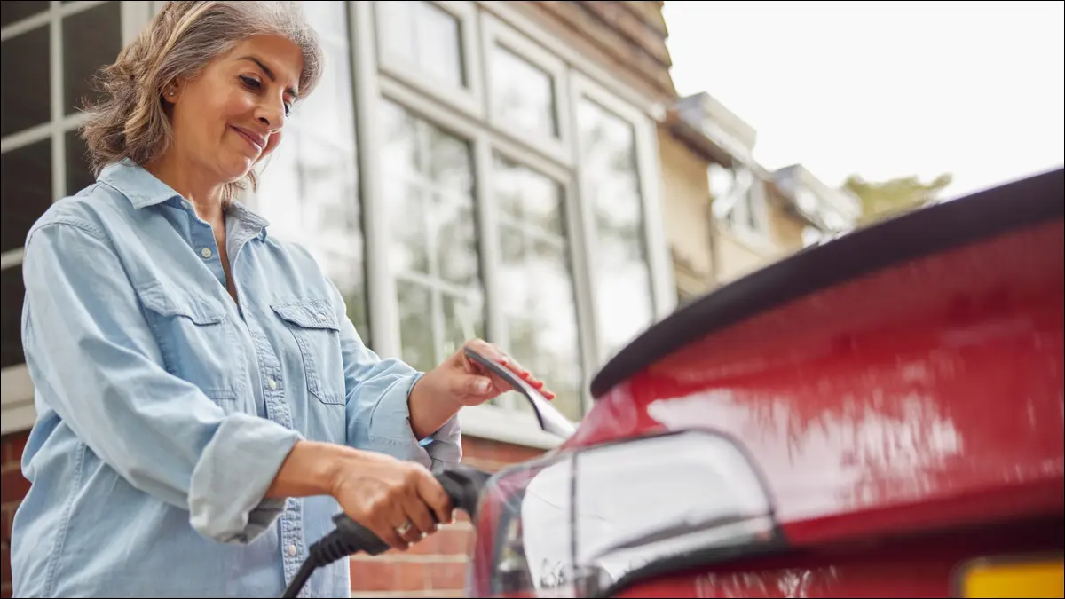 Femme chargeant une voiture électrique à la maison.