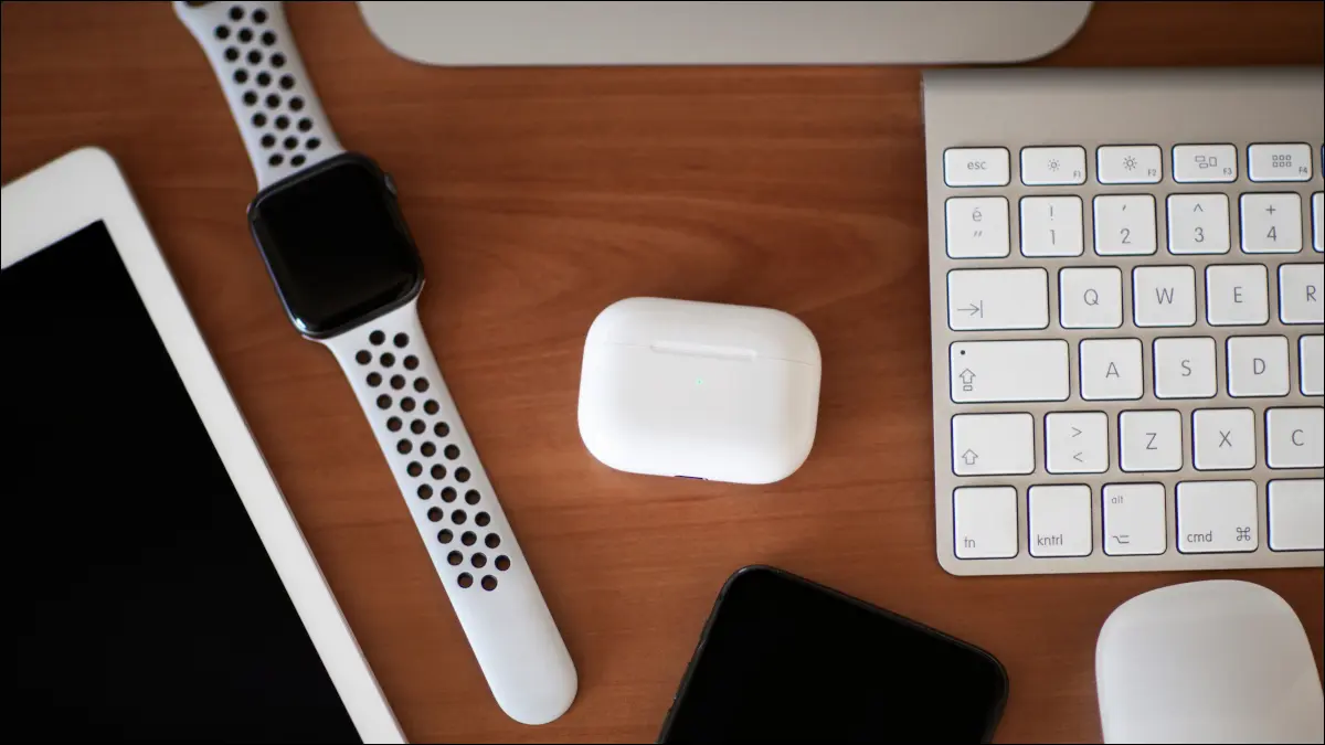 Чехол AirPods Pro на деревянной столешнице в окружении других устройств Apple.