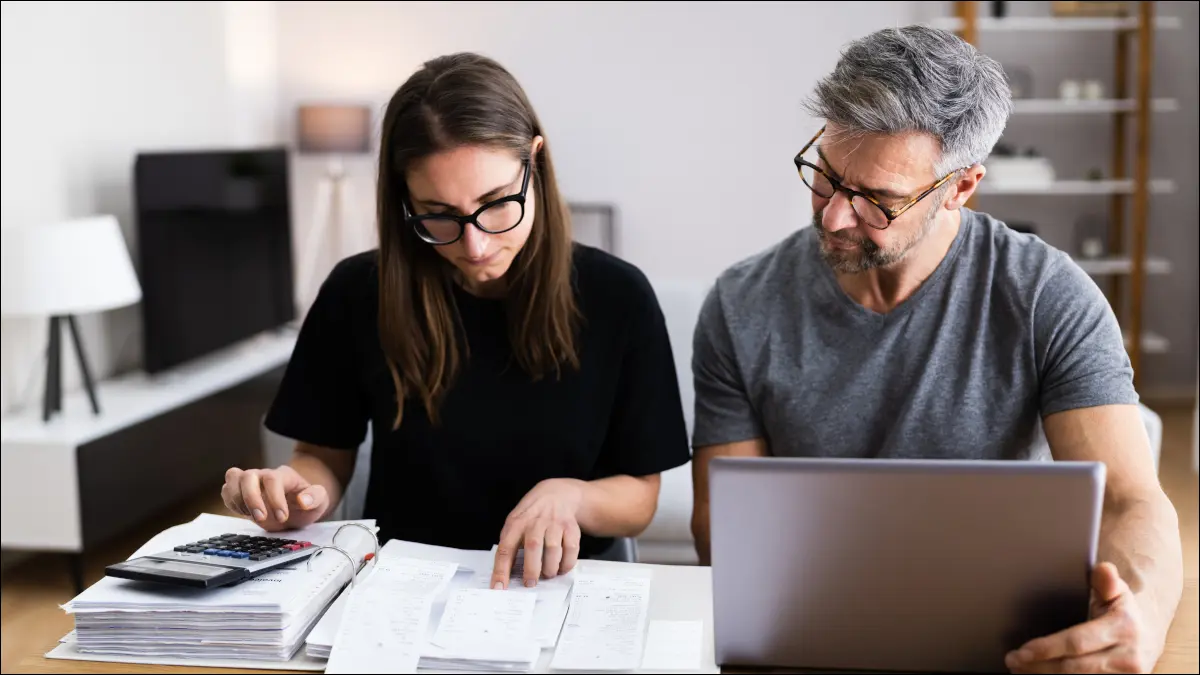 Una donna e un uomo che fanno le finanze con una calcolatrice, un taccuino e un computer portatile.