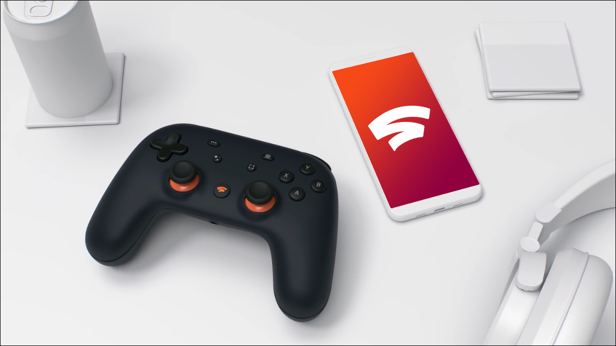 Google Stadia Founders 控制器坐在带有 Google Stadia 徽标的手机旁边的桌子上