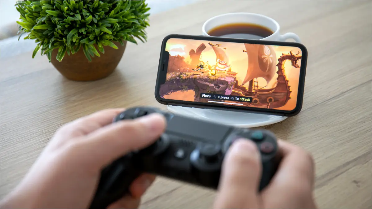 Person, die einen DualShock 4-Controller vor einem iPhone 11 hält und Rayman Adventures spielt.