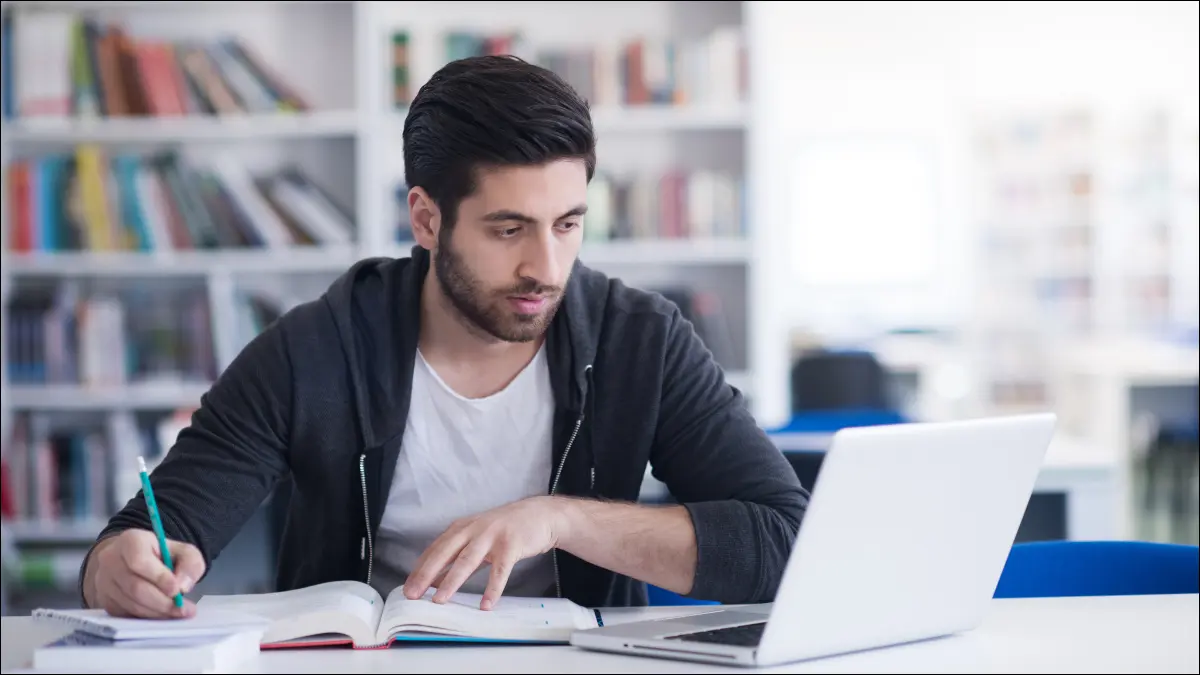 Jeune homme étudiant dans une bibliothèque et utilisant un ordinateur portable.