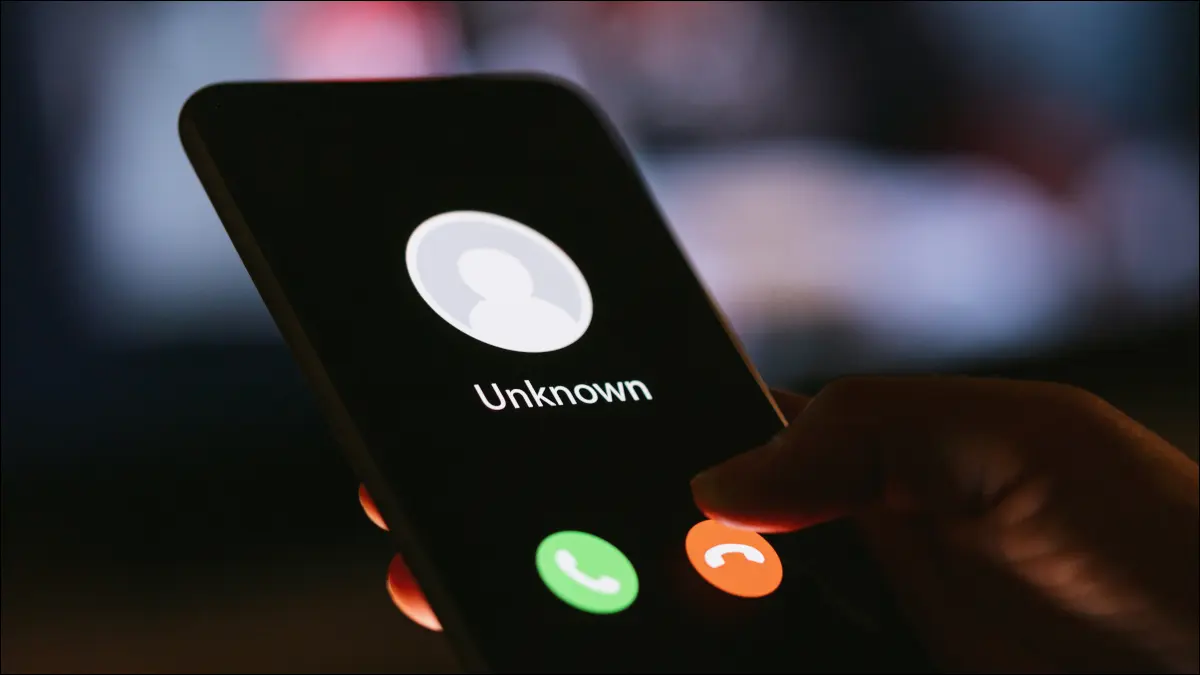 暗闇の中でスマートフォンを持っている人の手。見知らぬ発信者からの電話が表示されている。