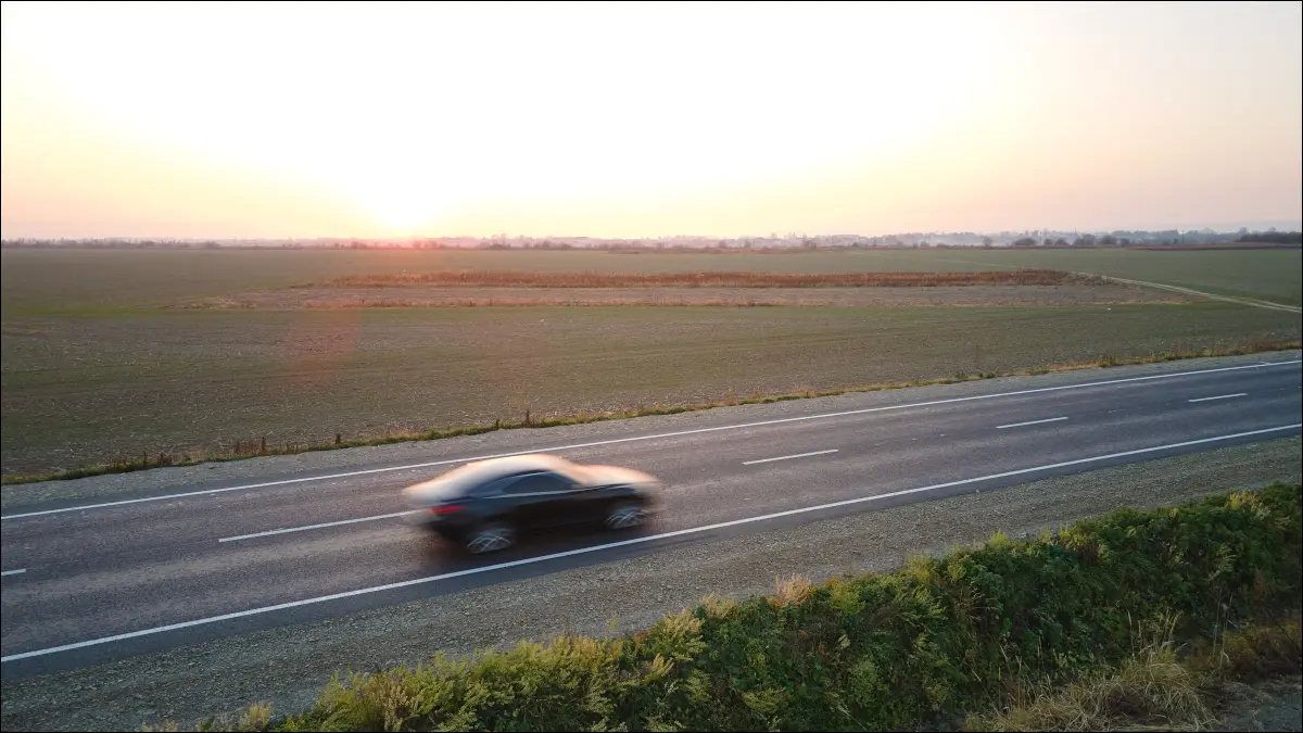 Vedere aeriană a unui vehicul electric care trece cu viteză pe o trecere a autostrăzii aruncă un câmp deschis la apus.
