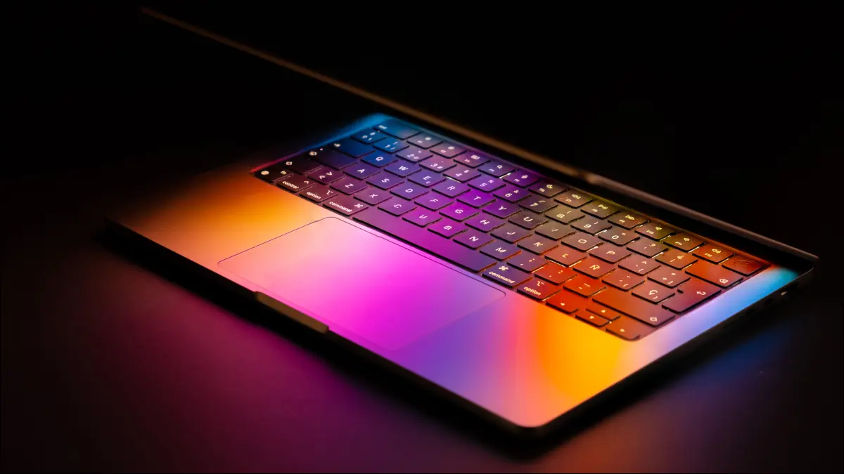 Una MacBook de Apple con la computadora portátil levantada parcialmente y la luz de la pantalla reflejada en el teclado.