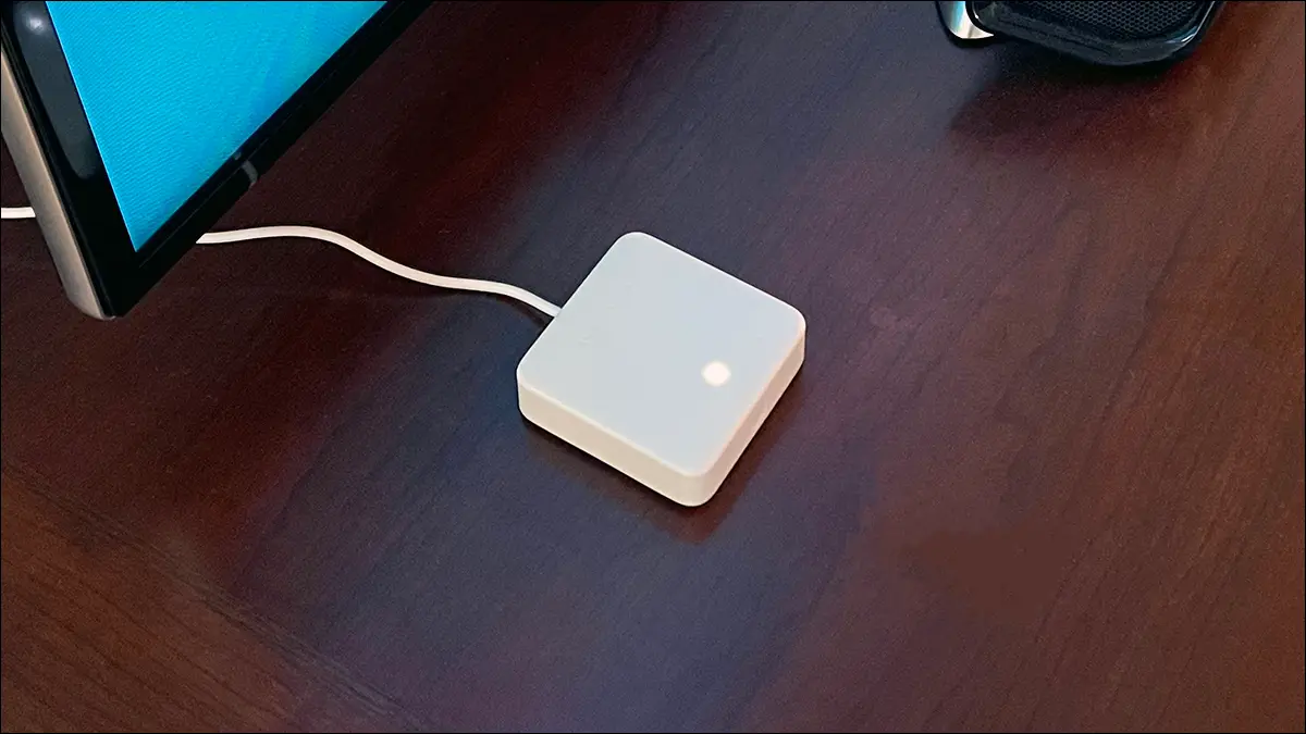 SwitchBot Hub Mini sur une table à côté d'un téléviseur et d'une barre de son