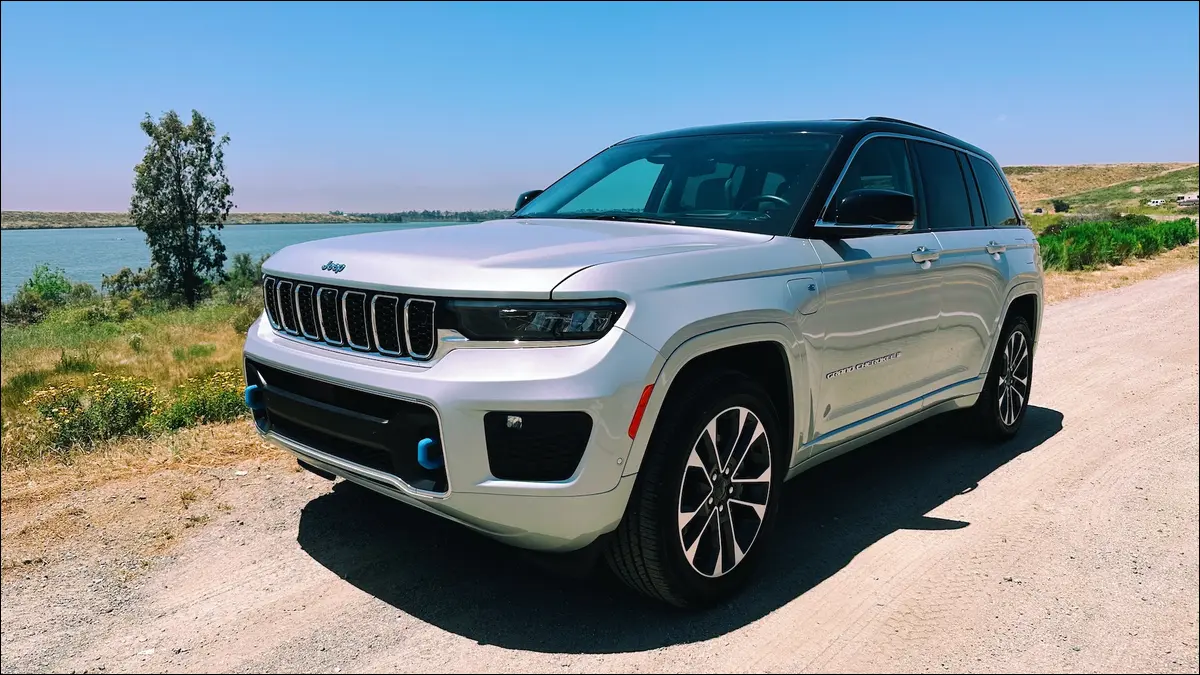 Вид спереди на Jeep Grand Cherokee Overland 4xe серебристого цвета на фоне озера