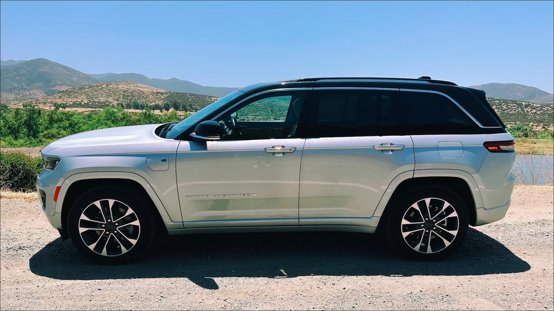 Вид сбоку на Jeep Grand Cherokee 4xe серебристого цвета на фоне озера.